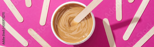 top view of depilation wax in container with sticks on pink background, panoramic shot
