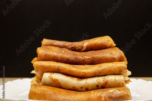 Many homemade thin pancakes with filling stacked pyramid on a white plate sideways against a black wall  copy space