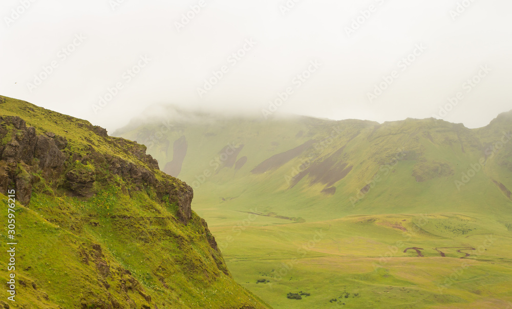 View over steep green mountains in fog, sloudy weather, haze over hills, Iceland