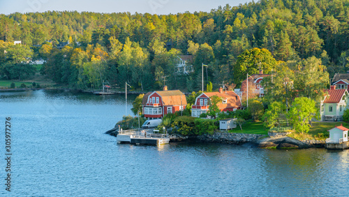Tableau sur toile Rocky coast of Stockholm archipelago in Baltic sea with traditional white and red houses at sunny autumn evening with a fall scenery