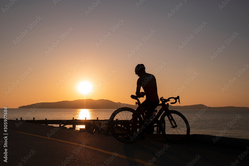 Fototapeta premium Silhouette people ride a bicycle,bicycle rider watching the sunrise over the mountain at sea
