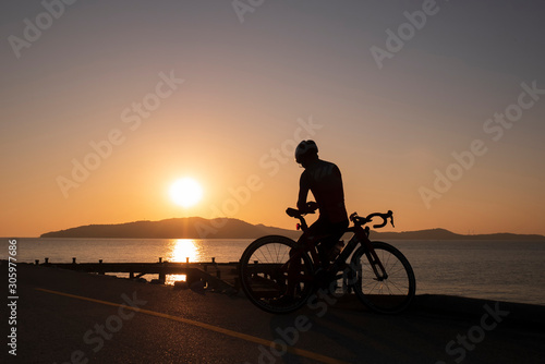 Silhouette people ride a bicycle,bicycle rider watching the sunrise over the mountain at sea
