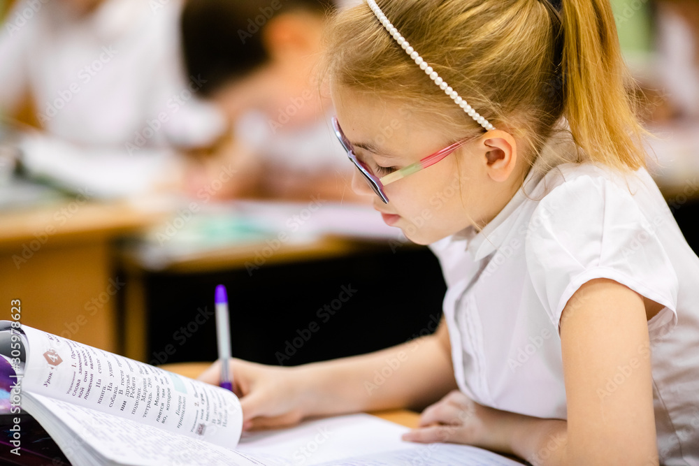 Blonde girl with big glasses sitting in classroom, studing, smiling. Education on elementary school, first day at school Blonde girl with big glasses sitting in classroom, studing, smiling. Education on elementary school, first day at school