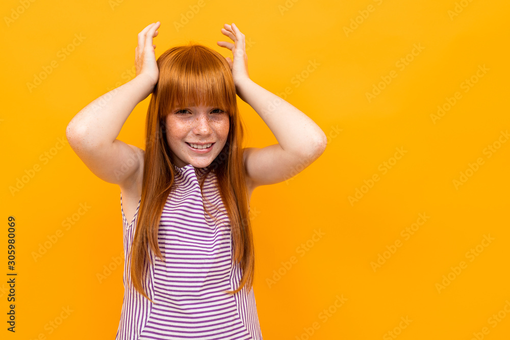 red-haired beautiful young girl in a T-shirt grimaces looking at the camera on a yellow background