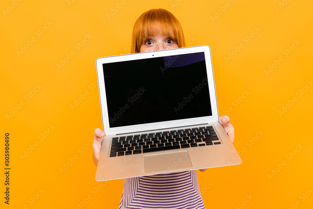 Red-haired girl demonstrates a laptop screen on a yellow background Red-haired girl demonstrates a laptop screen on a yellow background