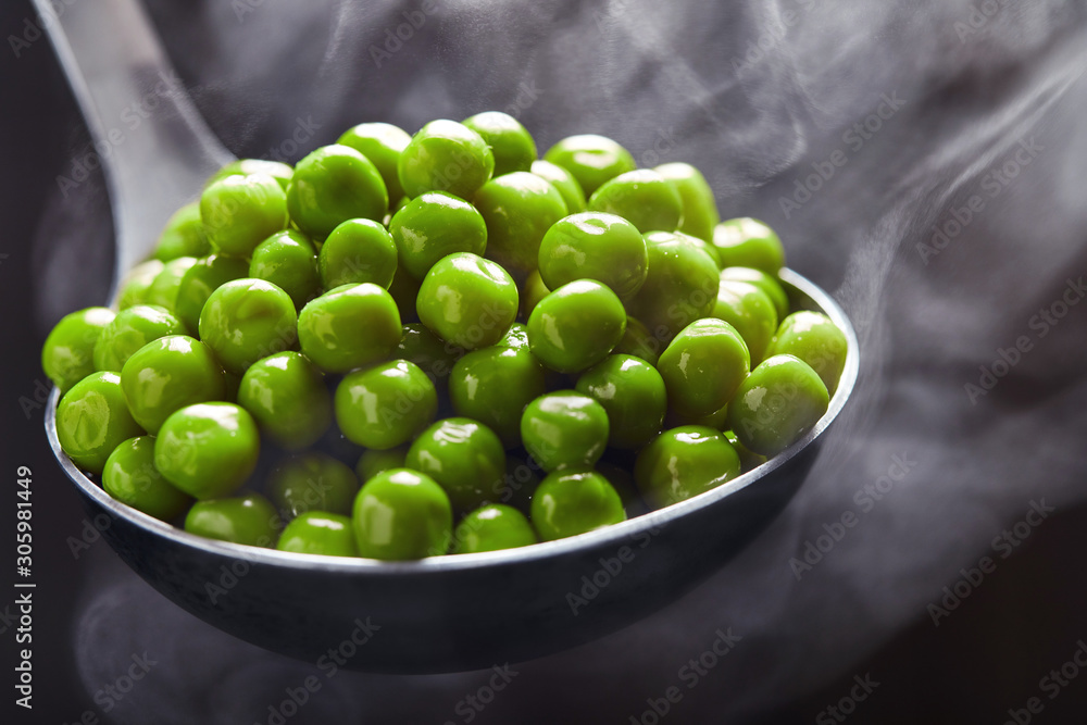 Green peas in a ladle with steam coming from it against a dark background. Close up Green peas in a ladle with steam coming from it against a dark background. Close up