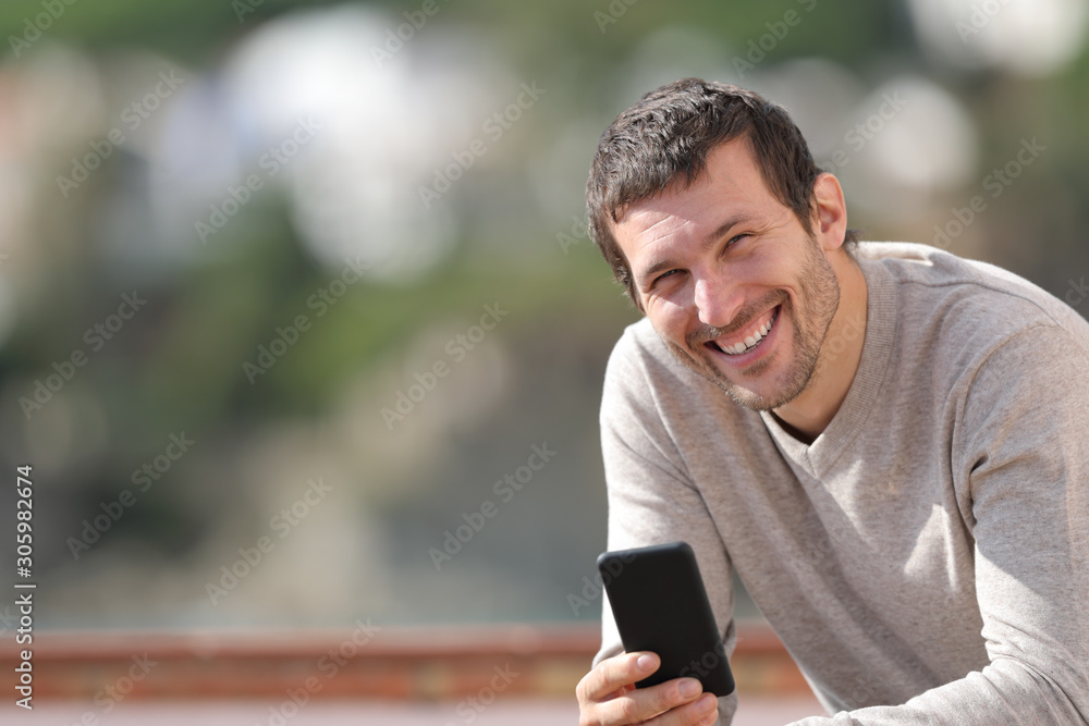 Happy adult man holding smart phone looks at camera Happy adult man holding smart phone looks at camera