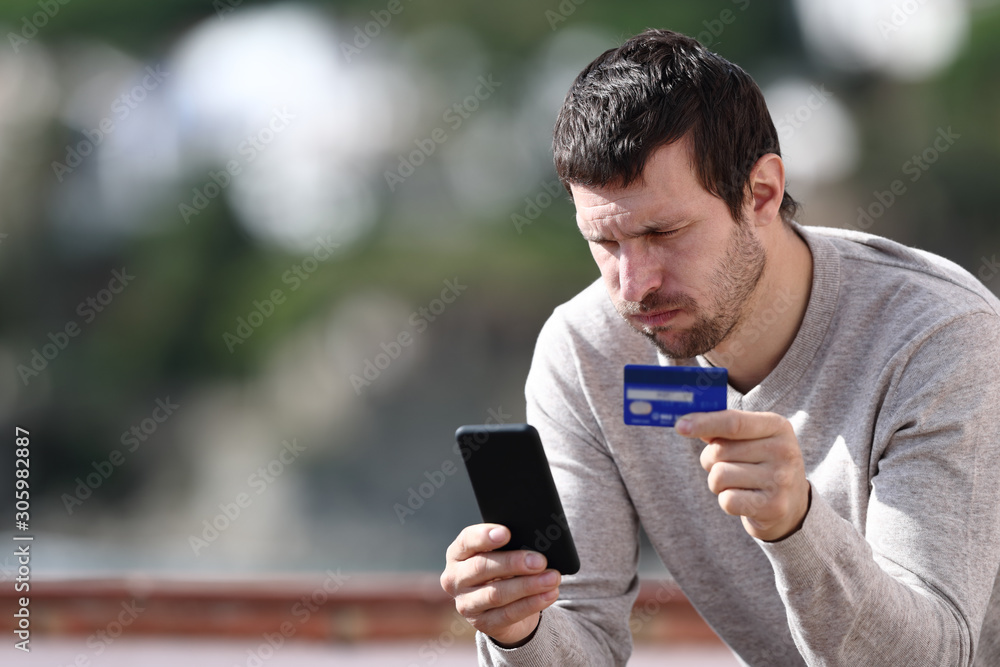Worried man buying online with credit card and phone Worried man buying online with credit card and phone