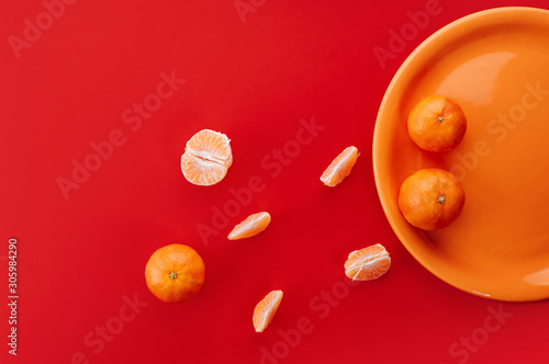 Tangerines on orange plate. Monochrome styled flat lay on bold red background.