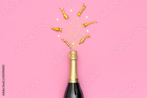Christmas and New Year background. Champagne bottle, festive golden ribbons and star confetti on pink background top view. Flat lay holiday card. Birthday or wedding concept. Festive decorations 2020