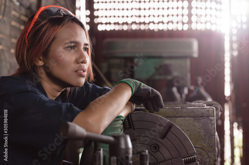 Exhausted Asian female engineer taking break on industrial machine - Diverse factory employee woman suffering depression worry and anxiety at work - Overtime, regulations and immigrant worker concept