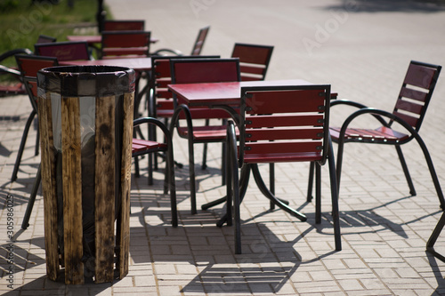 Outdoor bar. Wooden trash bin. Red tables and chairs in a summer cafe on the alley. © Omega