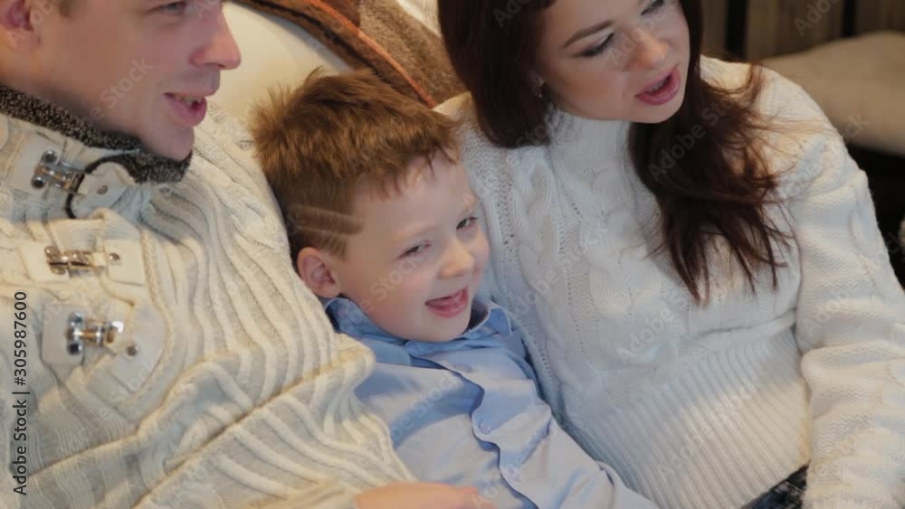Beautiful happy family of three on the sofa smiling and talking by the Christmas tree on Christmas night. Beautiful happy family of three on the sofa smiling and talking by the Christmas tree on Christmas night.