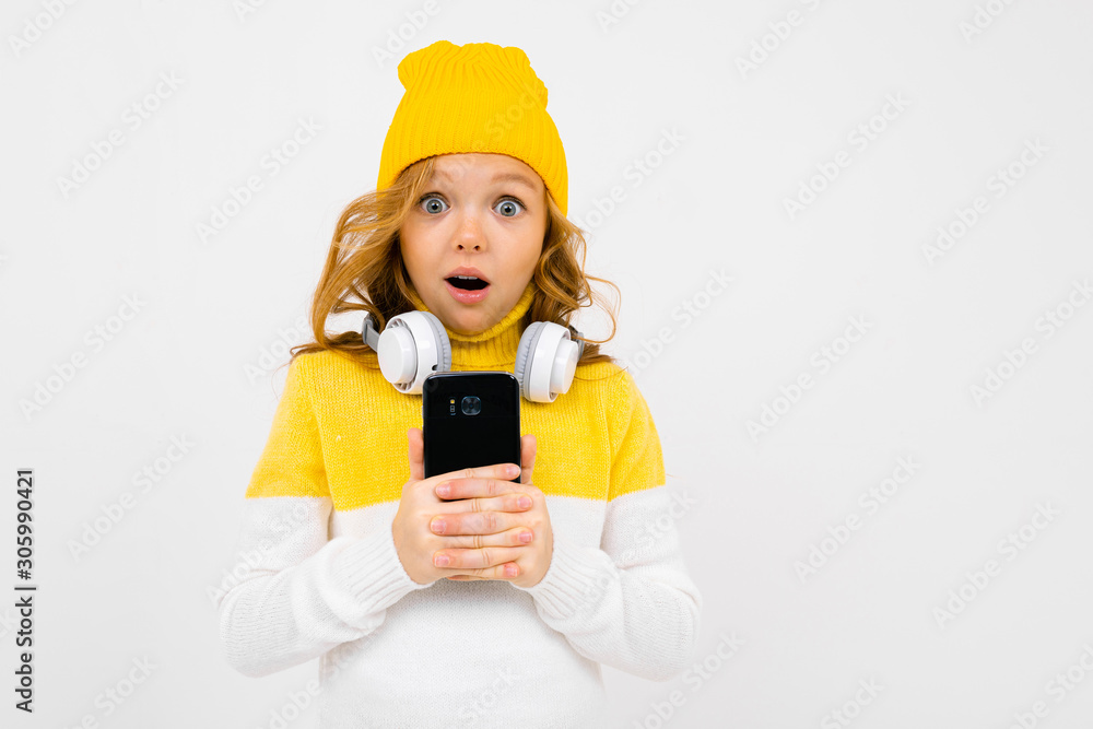 European cute girl with big headphones and smartphone listens to music and grimaces on a white studio background European cute girl with big headphones and smartphone listens to music and grimaces on a white studio background