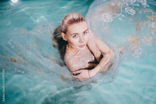Beautiful blonde girl in a white dress swims underwater in a pool with bubbles. Suitable for advertising. Red and white hair