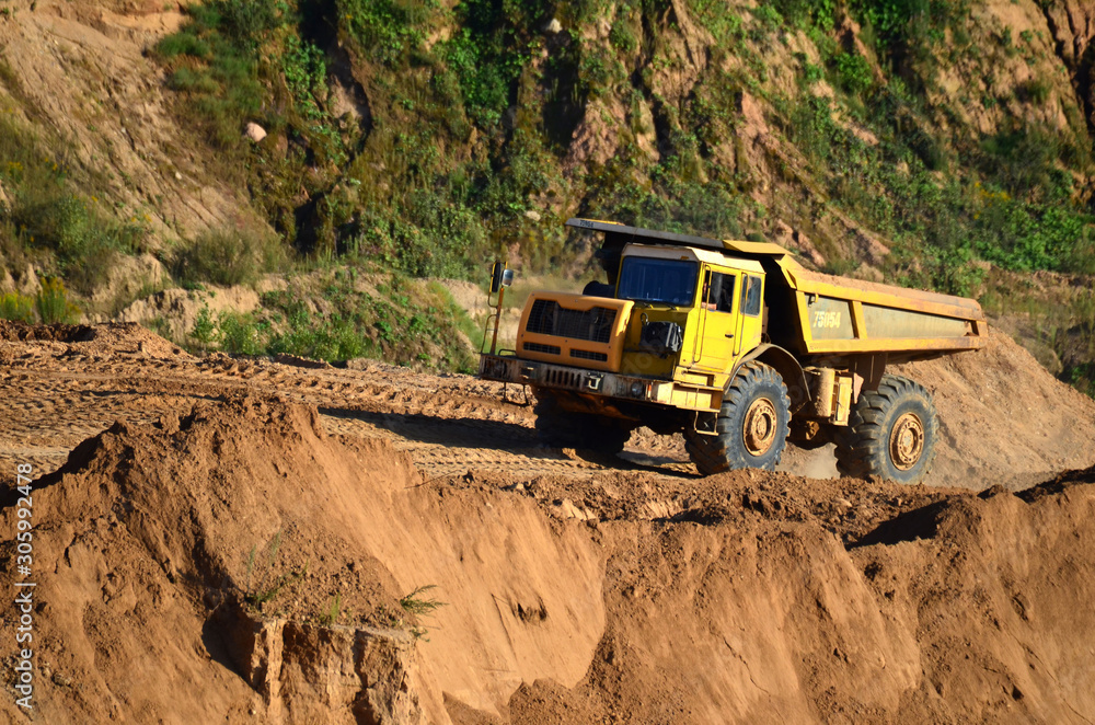 Big yellow dump truck transporting sand in an open-pit mining quarry. Mining quarry for the production of crushed stone, sand and gravel for use in the construction industry - image Big yellow dump truck transporting sand in an open-pit mining quarry. Mining quarry for the production of crushed stone, sand and gravel for use in the construction industry - image