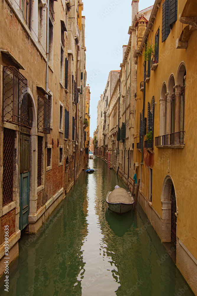 Long and narrow canal with emerald water between medieval buildings. Boats moored near walls. Picturesque landscape of Venice. Famous touristic place and travel destination in Europe. Venice, Italy