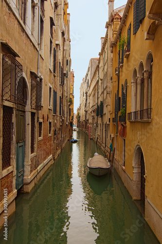 Long and narrow canal with emerald water between medieval buildings. Boats moored near walls. Picturesque landscape of Venice. Famous touristic place and travel destination in Europe. Venice  Italy