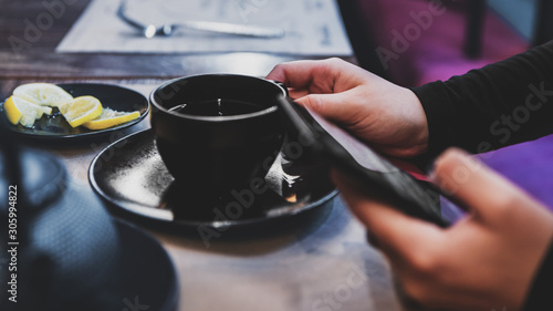 woman hand using mobile phone at a cafe with tea cup on table