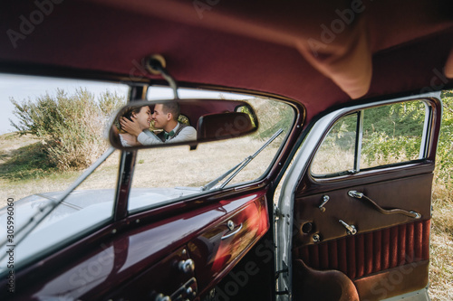 Smiling and in love newlyweds hug, and are reflected in the rear view mirror of an expensive car in the interior. Wedding portrait of a stylish bride and groom. Photography, concept.