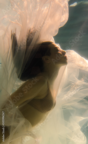 Beautiful girl swims underwater with long hair. Blue or gold background like gold. The atmosphere of a fairy tale or magic. Diving under the water with a shiny cloth © Underwater girls