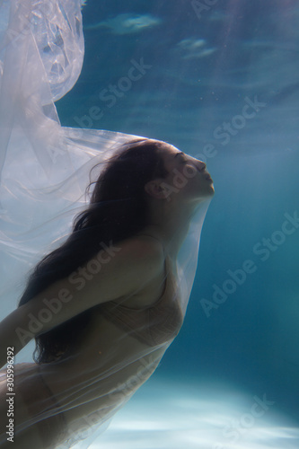 Beautiful girl swims underwater with long hair. Blue or gold background like gold. The atmosphere of a fairy tale or magic. Diving under the water with a shiny cloth