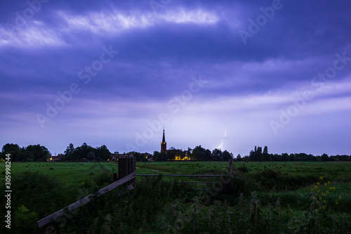Lightning storm strikes near a small village at in in farmland