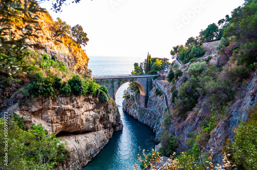 View on Fiordo di Furore arc bridge built between high rocky cliffs above the Tyrrhenian sea bay in Campania region. Curved walkway on the mountain around the unique nature gorge