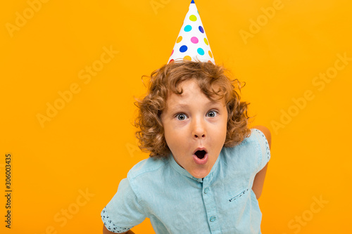 European red-haired curly boy with a festive cap is grimacing at the camera isolated yellow background