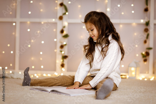 Happy little child girl is reading fairy tale book on the background with lights. Merry Christmas. space for text © producer