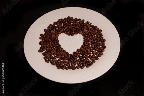 In love with coffee. Coffee is in my heart. Coffee beens spilled in heart shape on white plate.