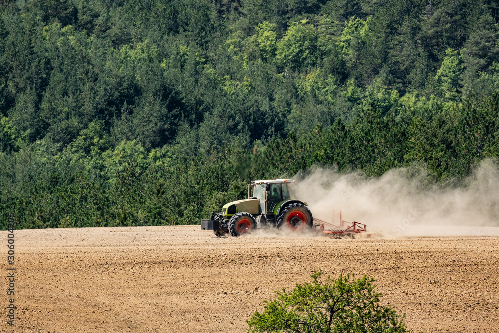 Obraz premium tractor plows a field near forest