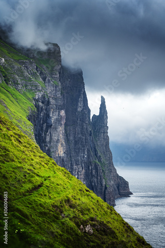 Gorgeous faroese landscape with famous Witches Finger cliffs and dramatic cloudy sky from Trollkonufingur viewpoint. Vagar island, Faroe Islands, Denmark.