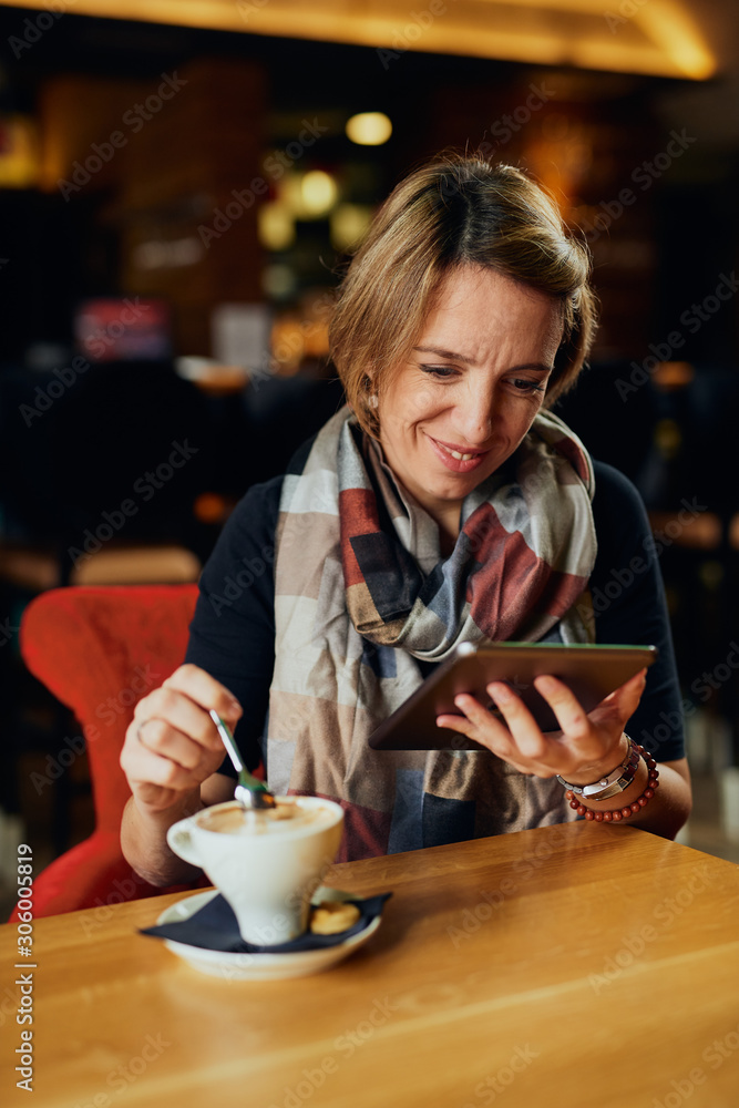 Beautiful Caucasian woman with coffee  looking at her tablet