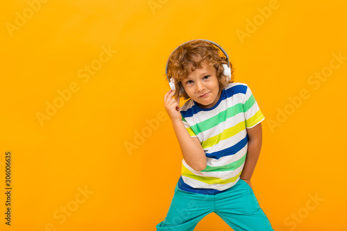 Red-haired curly boy listens to music in large headphones on a yellow background