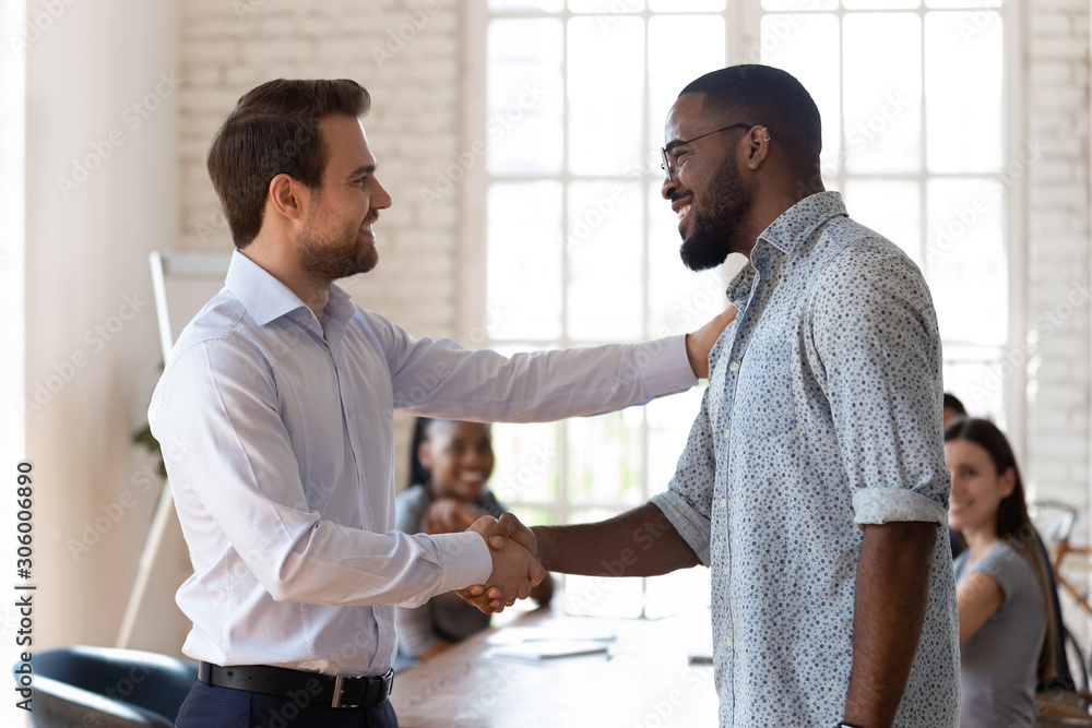 Confident company director shaking hands with happy african american employee.