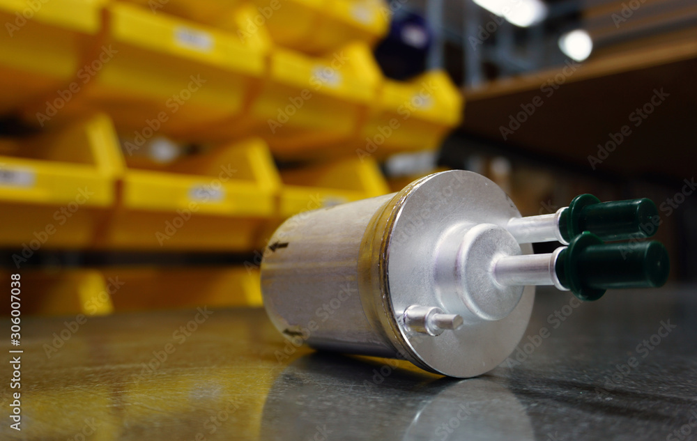 Concept new high quality original spare parts. New original fuel filter on blurry background of a storage rack. New original spare parts as a guarantee of quality, durability, reliability. Concept new high quality original spare parts. New original fuel filter on blurry background of a storage rack. New original spare parts as a guarantee of quality, durability, reliability.