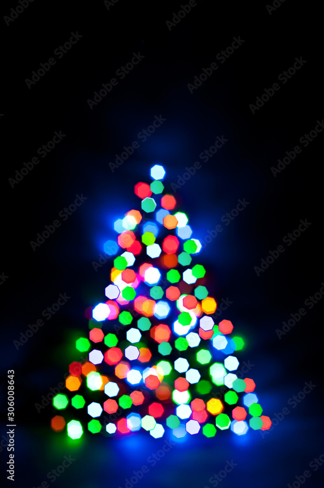 Christmas fairy lights are defocused in the shape of a fir tree, giving a blurry effect. Dark background for design. Christmas fairy lights are defocused in the shape of a fir tree, giving a blurry effect. Dark background for design.