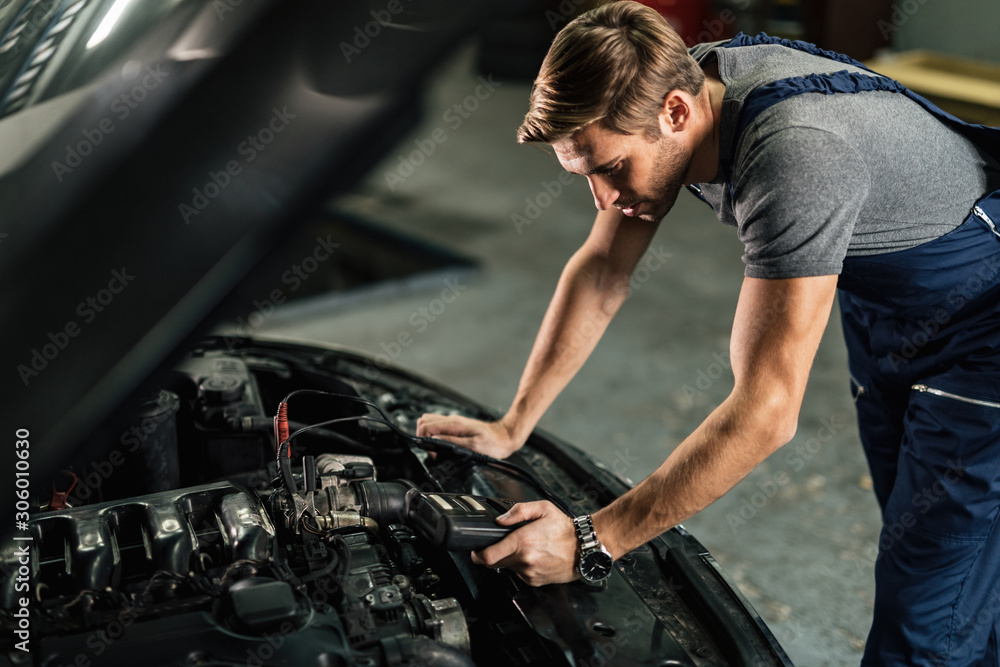 Young car mechanic using diagnostic tool while working in auto repair shop.