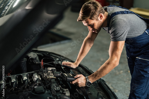Young car mechanic using diagnostic tool while working in auto repair shop.