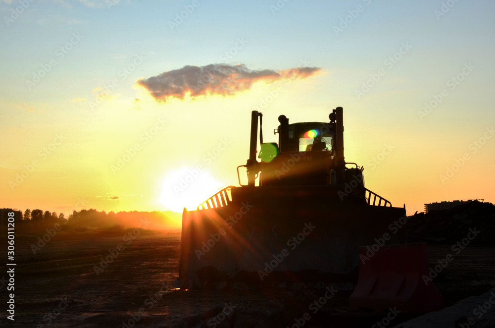 Silhouetted bulldozer on the background of the rays of the sun at sunset at a construction site. Land clearing, grading, pool excavation, utility trenching, utility trenching and foundation digging Silhouetted bulldozer on the background of the rays of the sun at sunset at a construction site. Land clearing, grading, pool excavation, utility trenching, utility trenching and foundation digging