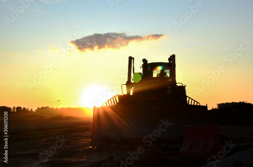 Silhouetted bulldozer on the background of the rays of the sun at sunset at a construction site. Land clearing, grading, pool excavation, utility trenching, utility trenching and foundation digging © MaxSafaniuk