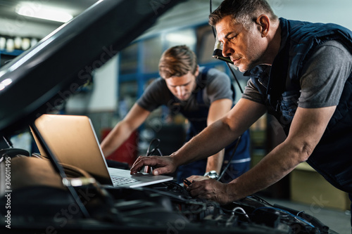 Auto mechanic using laptop while working on car diagnostic with his coworker.