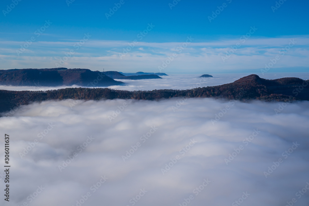 Germany, Beautiful aerial view above endless sea of fog clouds in valley of swabian alb nature landscape on a sunny day with blue sky near stuttgart