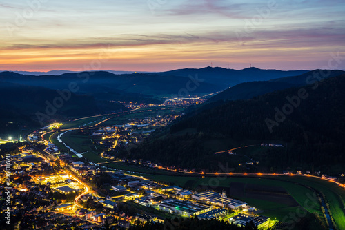 Germany, Black forest houses of city haslach im kinzigtal, streets and cityscape illuminated by night, aerial view from above with red sky, a perfect nature landscape surrounding the village