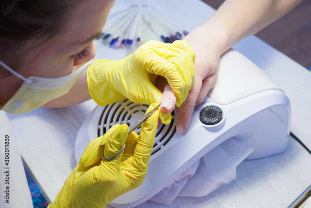 A qualified nail service specialist in protective rubber gloves removes the cuticle to the client