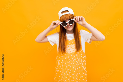 red-haired girl in sunglasses grimaces at the camera on a yellow background © Ivan Traimak