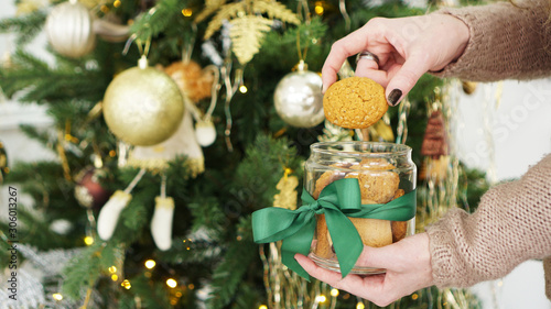 Oat cookies in a glass jar. Against the background of Christmas decor and Christmas tree in green and gold color