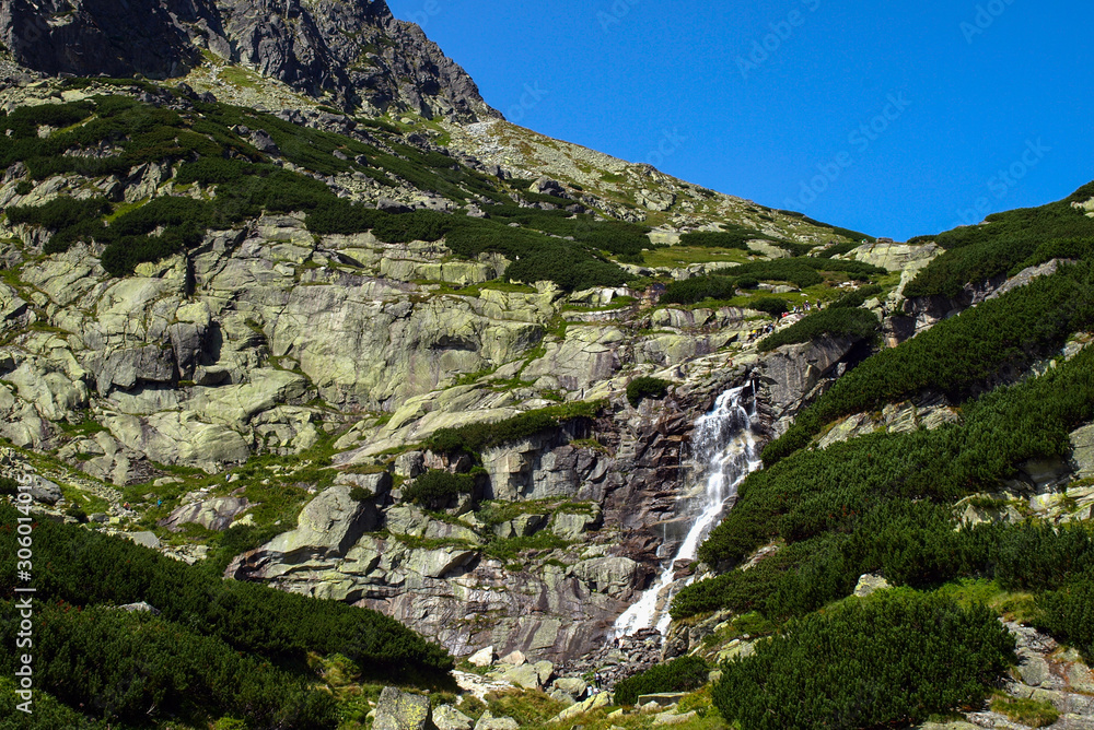 Rocky mountain path with waterfall and blue sky