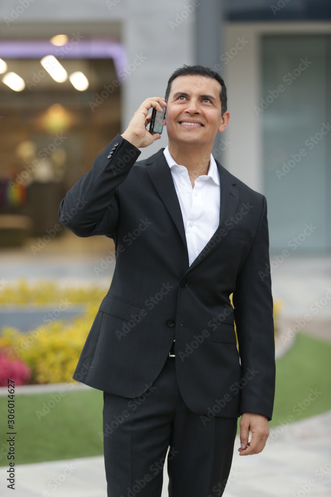 Handsome Latino executive man leaving office, talking on the phone and wearing casimir suit Handsome Latino executive man leaving office, talking on the phone and wearing casimir suit